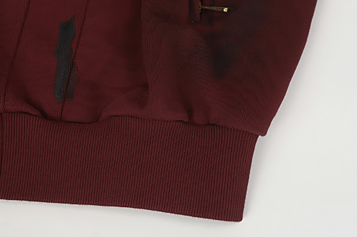Close-up of burgundy hooded zip-up sweatshirt showing ribbed hem and hand-painted graffiti detail