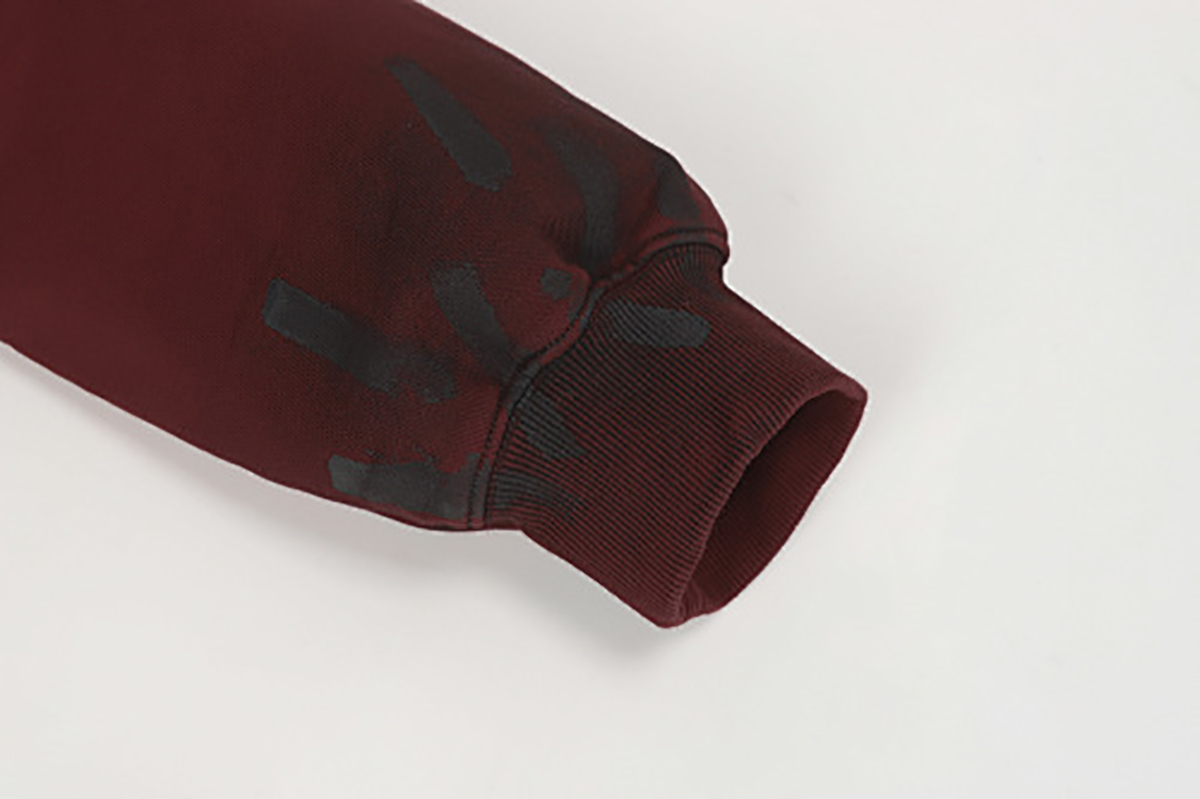 Close-up of burgundy hooded zip-up sweatshirt showing sleeve graffiti detail and ribbed cuff