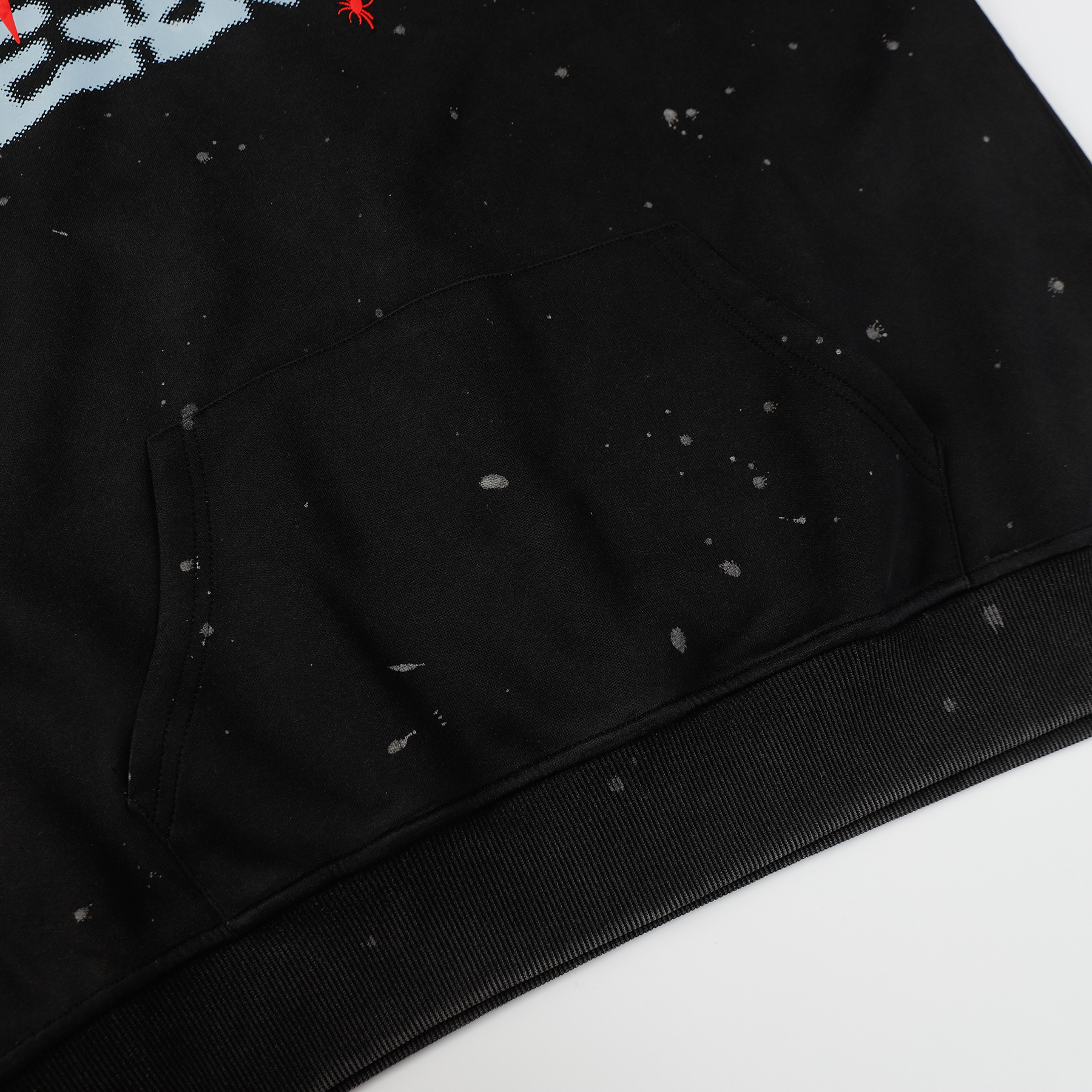 Hem detail of black spider puff print hoodie, showing hand-painted splatter effect and ribbed hem construction