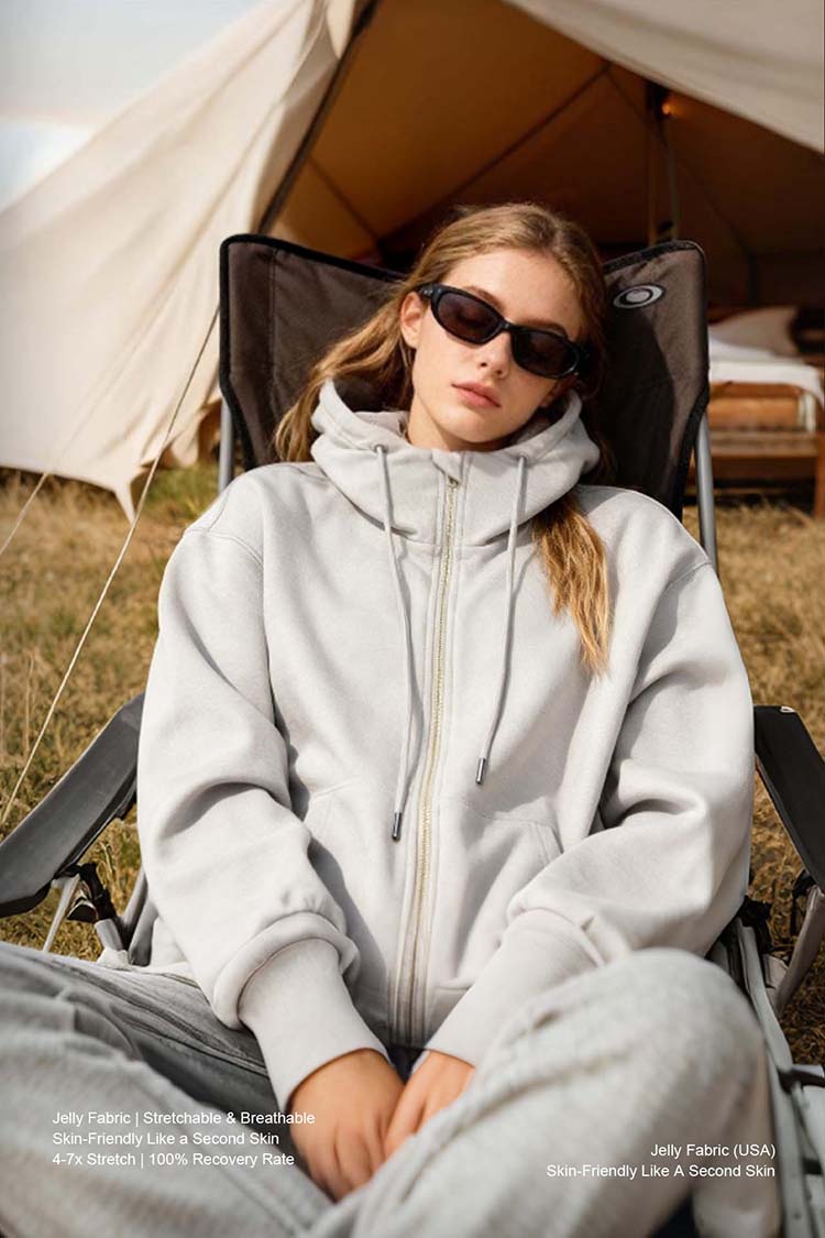 Woman wearing light gray inflatable hoodie relaxing at campsite, outdoor lifestyle shot